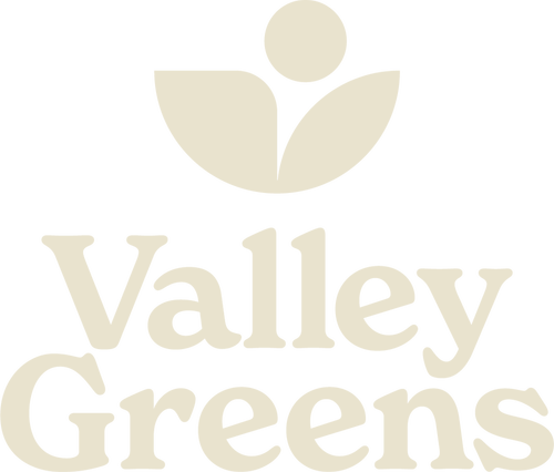 A minimalist logo for 'Valley Greens' featuring a serif font. Above the text is a geometric icon resembling a blooming plant or flower made of three rounded petals and a circle.